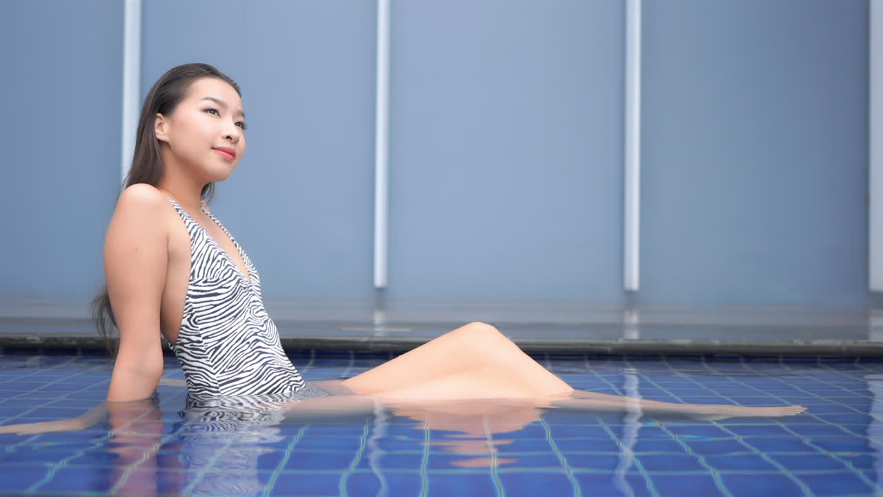 호텔 수영장의 물에서 즐기는 수영복에 젊은 몸집이 작은 아시아 여자
