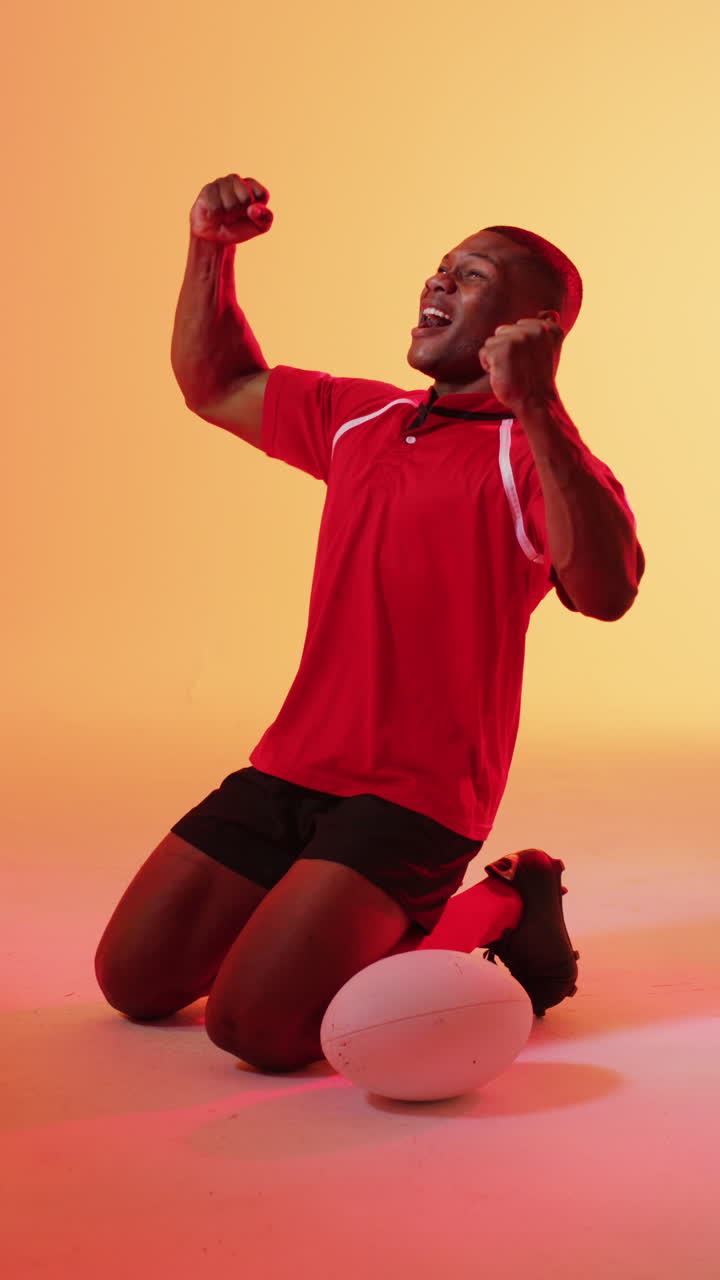 video vertical de un feliz jugador de rugby afroamericano levantando las manos sobre la iluminación rosa