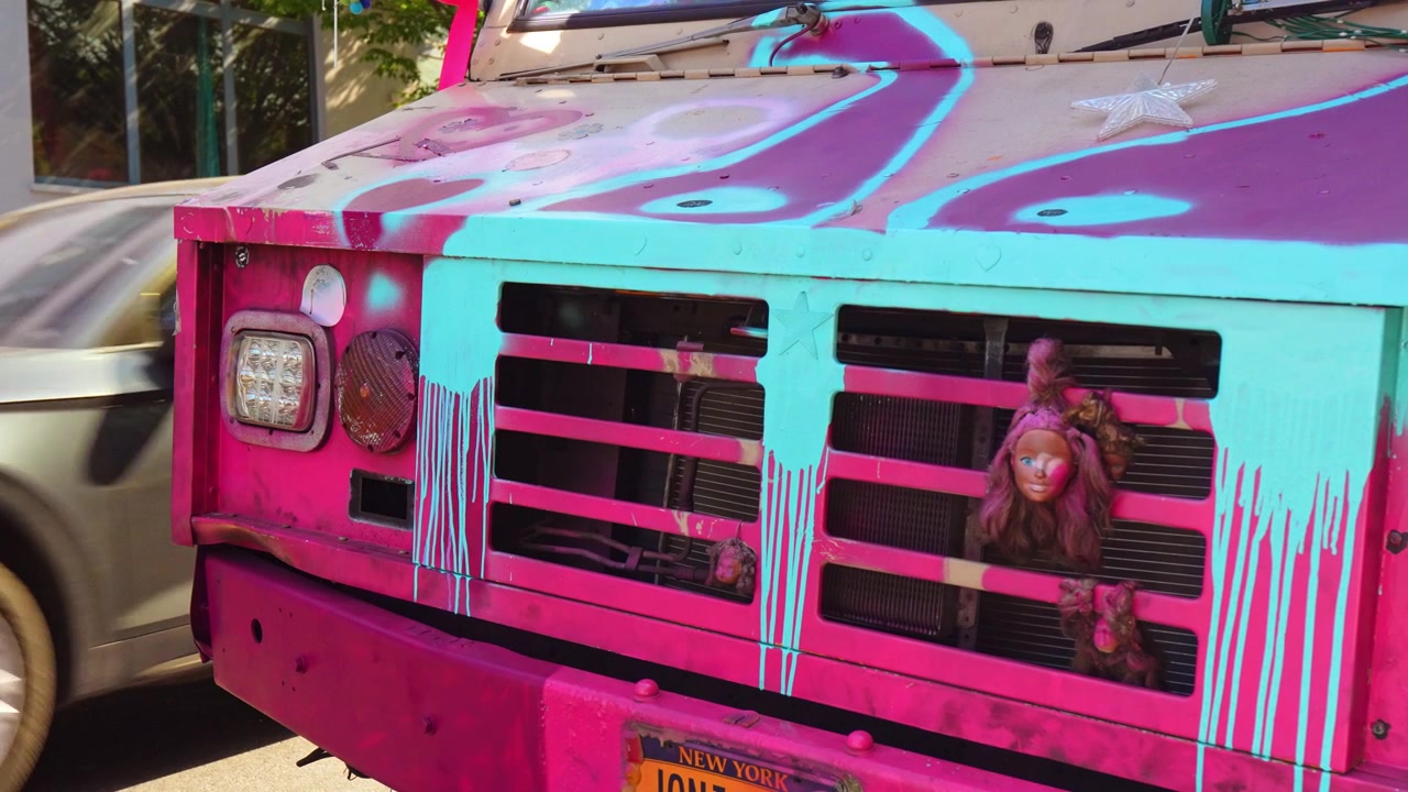 New York, USA, 26 May 2026: Close up of a pink painted bus front with doll in grille, New York. Detail shot of magenta and turquoise drip paint, star ornament and license plate.