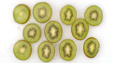 Water-splashes-in-slow-motion.-Top-view:-several-circles-of-kiwi-is-washed-with-water-on-a-white-background.-chopped-fruit.