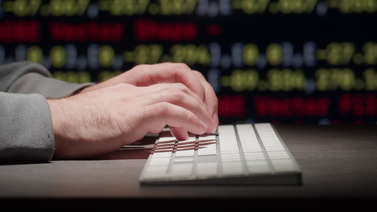 persona escribiendo en un teclado frente a un monitor que muestra datos