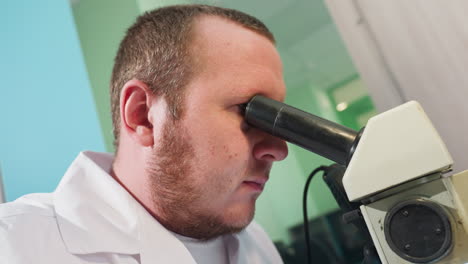 a close-up view of a focused technician using a microscope to examine intricate details, the technician wears a lab coat