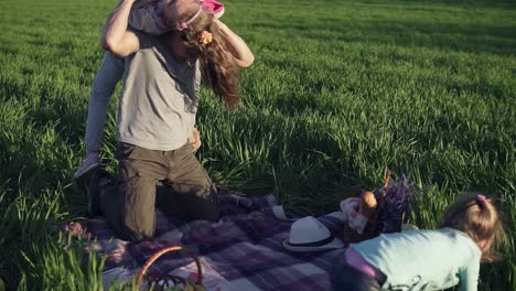 a young parent plays with his grown-up daughters in a meadow, on a litter. he throws the older one over his shoulder. the younger one playfully jumping on daddys back. slow motion