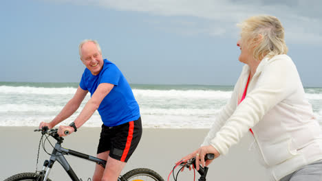 vista lateral de una vieja pareja caucásica montando en bicicleta en la playa 4k