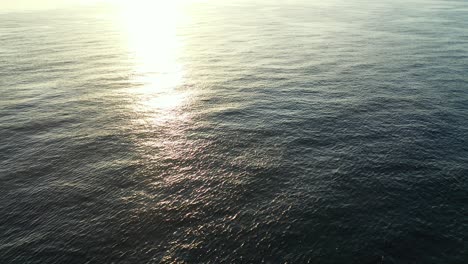 Flying-aerial-over-a-vast-body-of-water,-with-the-beautiful-afternoon-sun-glistening-in-the-ripples