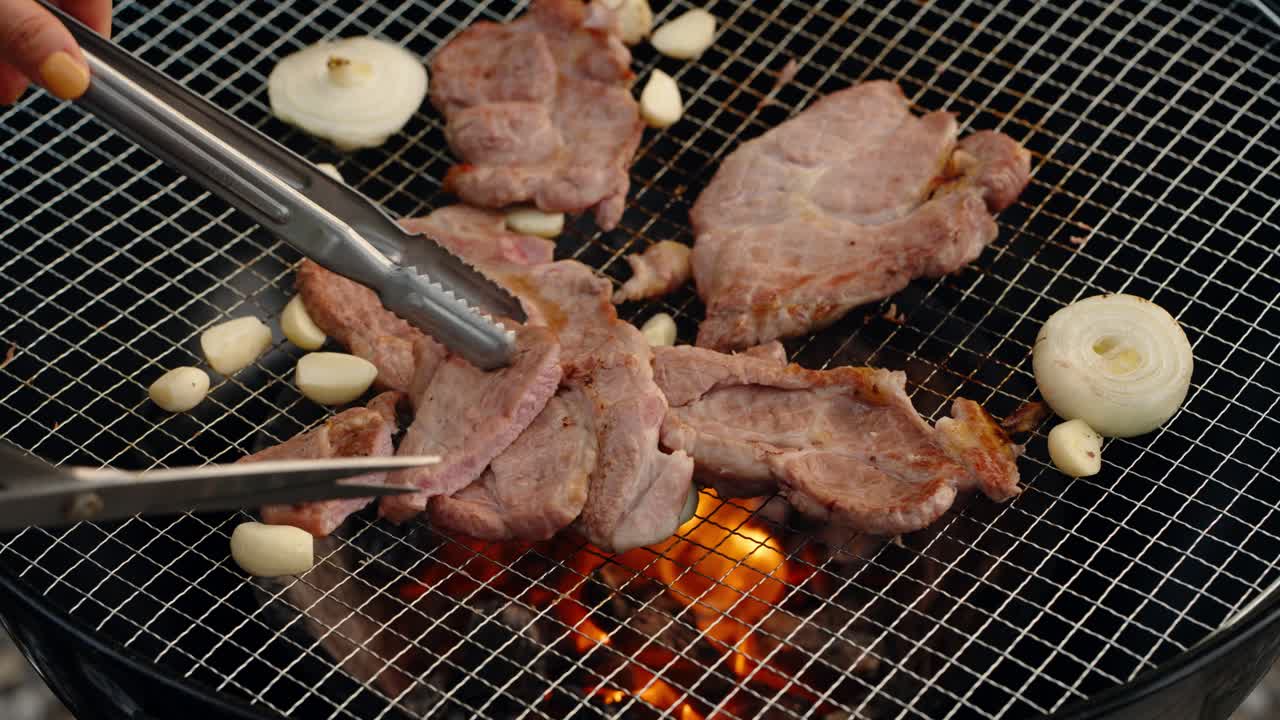 Close-up of a woman's hands using kitchen scissors to cut delicious grilled pork slices into bite-sized pieces directly on a hot charcoal barbecue, Korean style