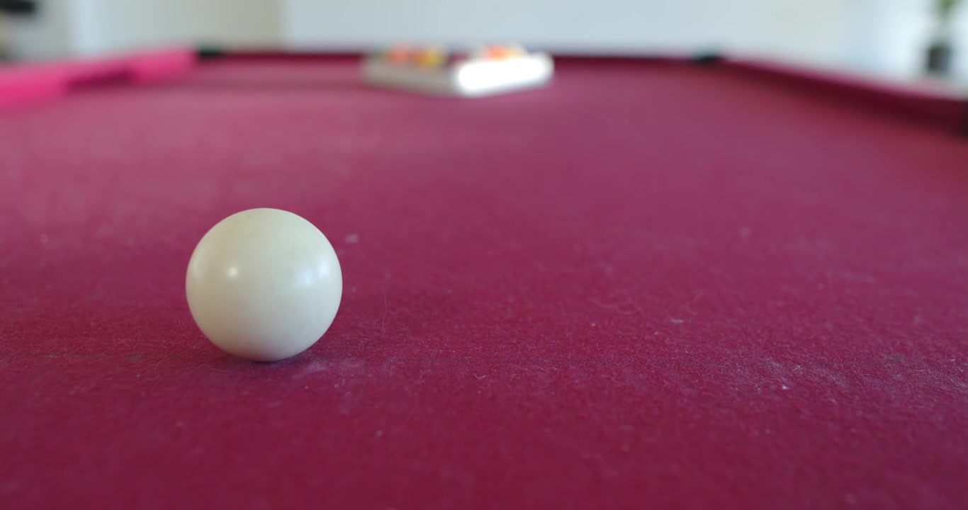 Camera is pulling back and shifting focus, revealing white spherical ball on magenta felt surface
