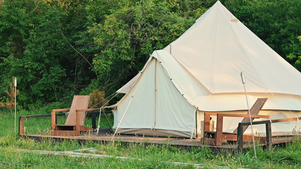 Tent with wooden chairs in front of it at glamping, lush forest around