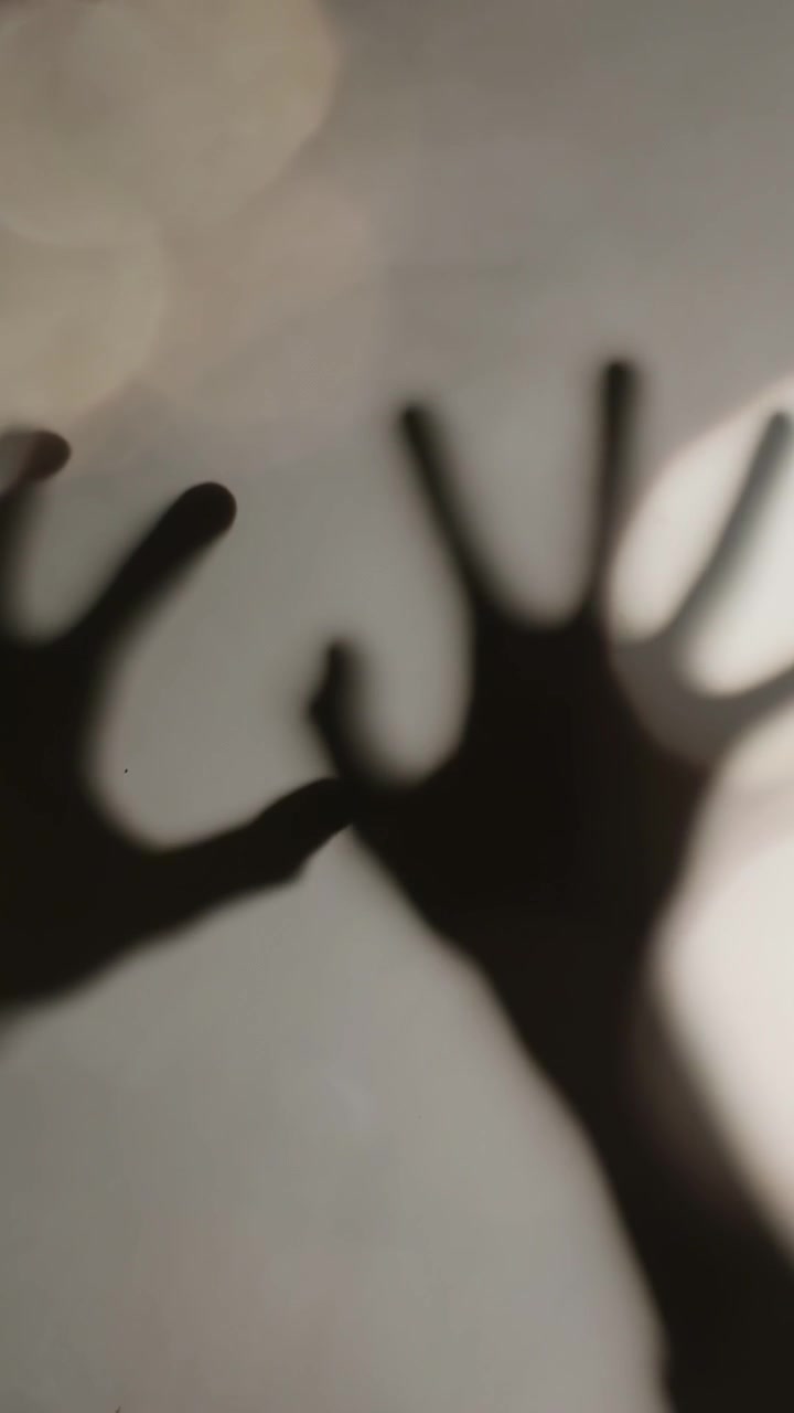 Video verticale: Controluce che proietta un'ombra, due mani che si protendono, scivolano ed esplorano una superficie satinata.