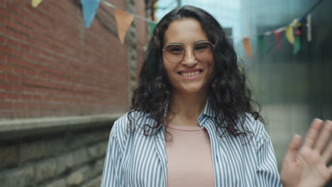 smiling woman waving in an urban alley