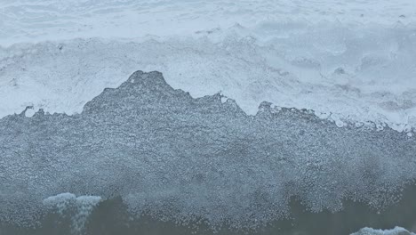 Suaves-Olas-Rompiendo-En-La-Orilla-De-Un-Lago-Congelado,-La-Calma-De-Un-Día-Frío-Capturada-En-Tonos-De-Azul