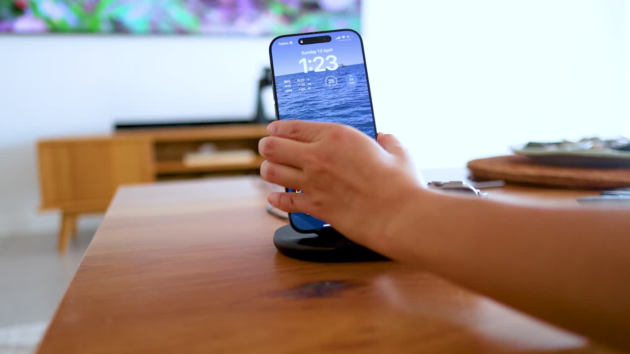 A smartphone is placed on a wireless charging dock in a bright, modern living room setting with minimalistic decor