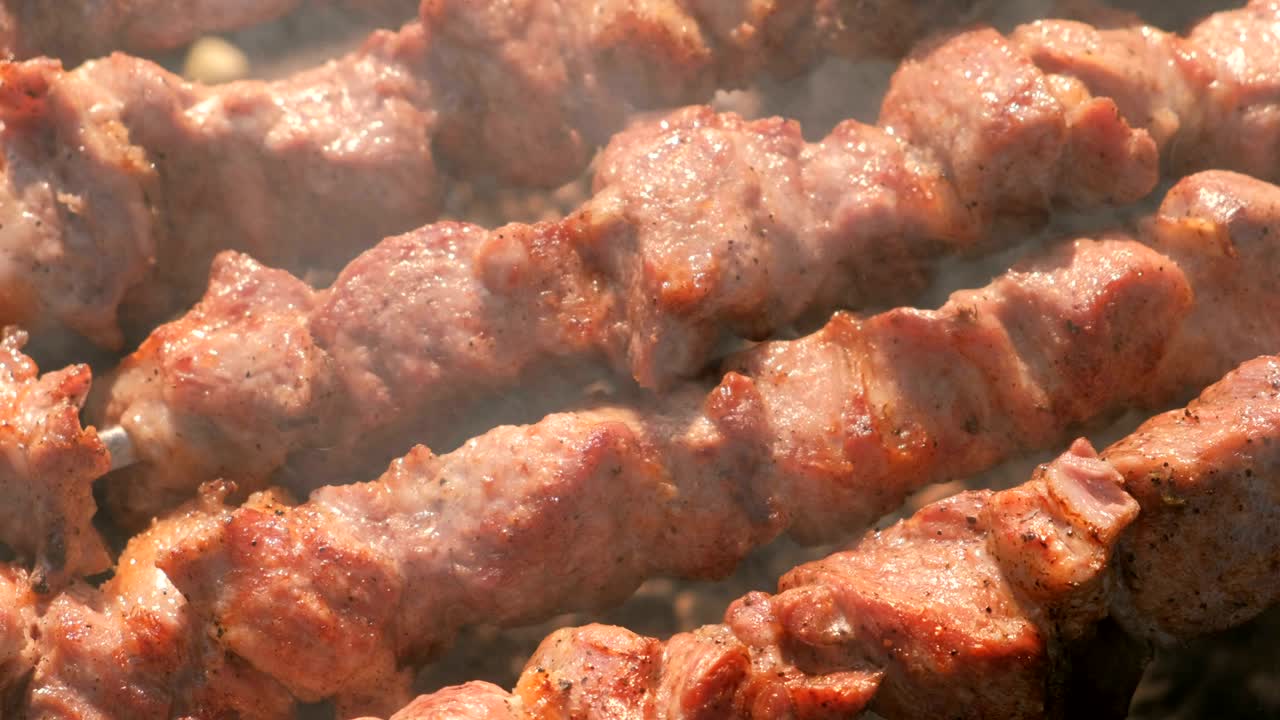 Appetizing juicy pork barbecue is roasted on skewers on top of charcoal grill. Close-up meat pieces.