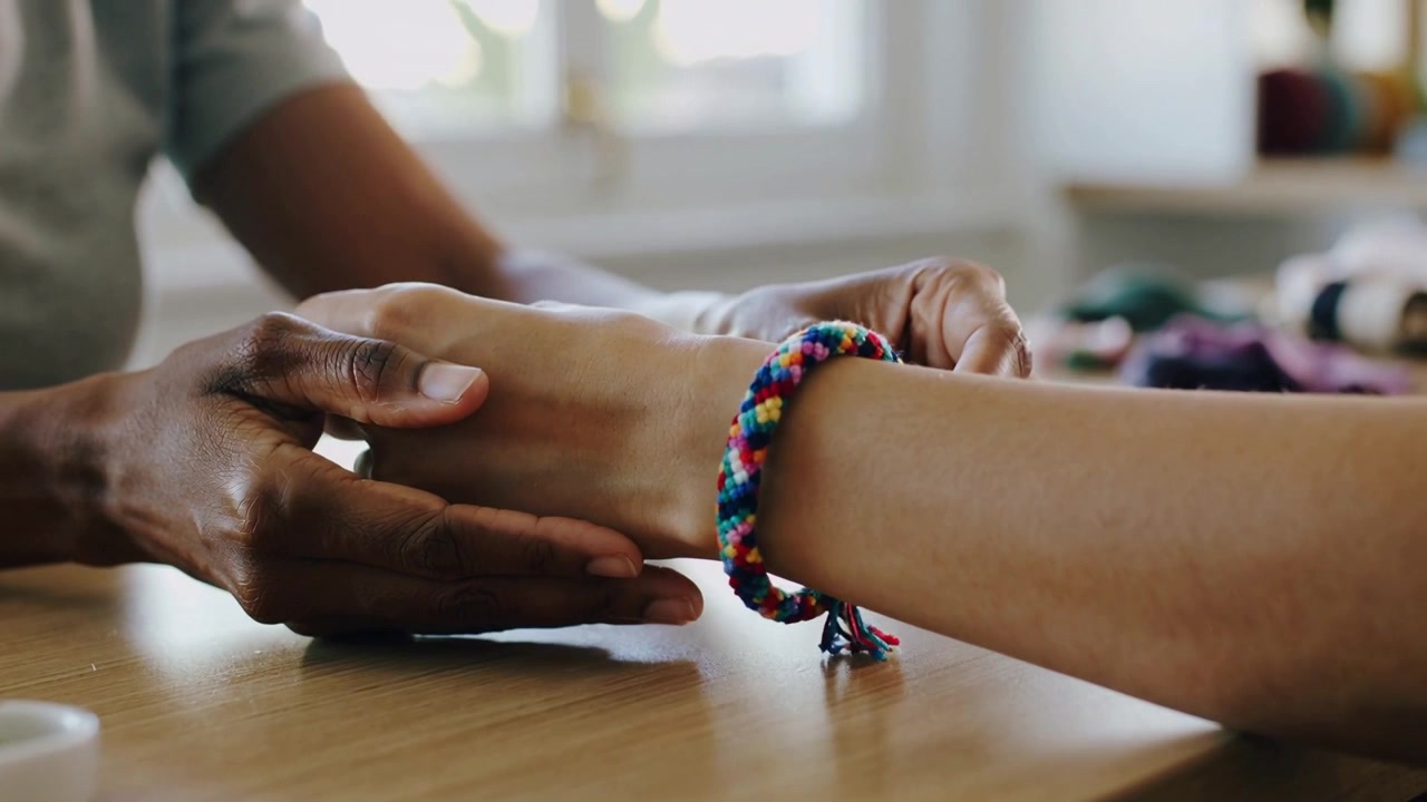 Tangan orang dewasa meraih memandu gelang kepang warna-warni ke pergelangan tangan di meja, membantu anak mengikat simpul