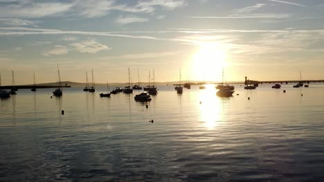 boats silhouetted on golden shimmering harbour ocean surface aerial view low circling right