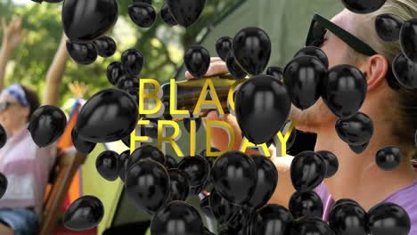 black friday text and black balloons animation over people enjoying outdoor event