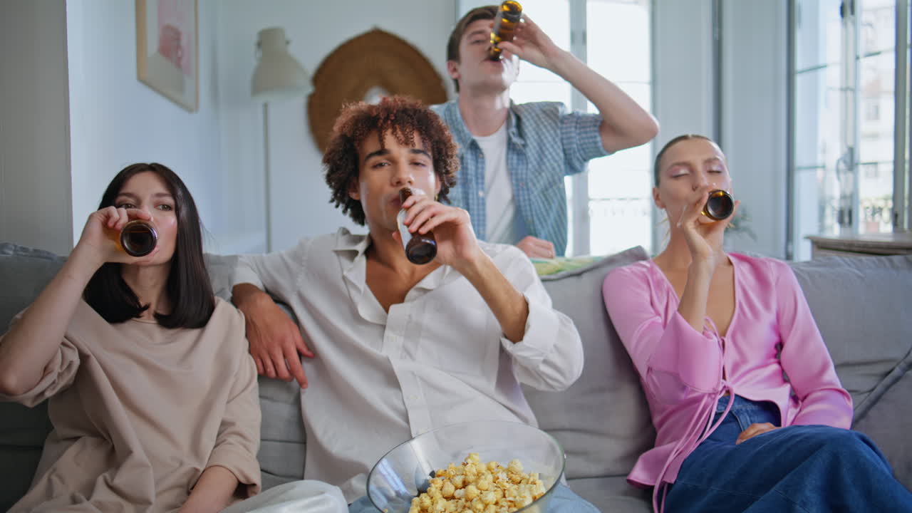 Carefree friends raising bottles toasting at cozy living room. People chilling