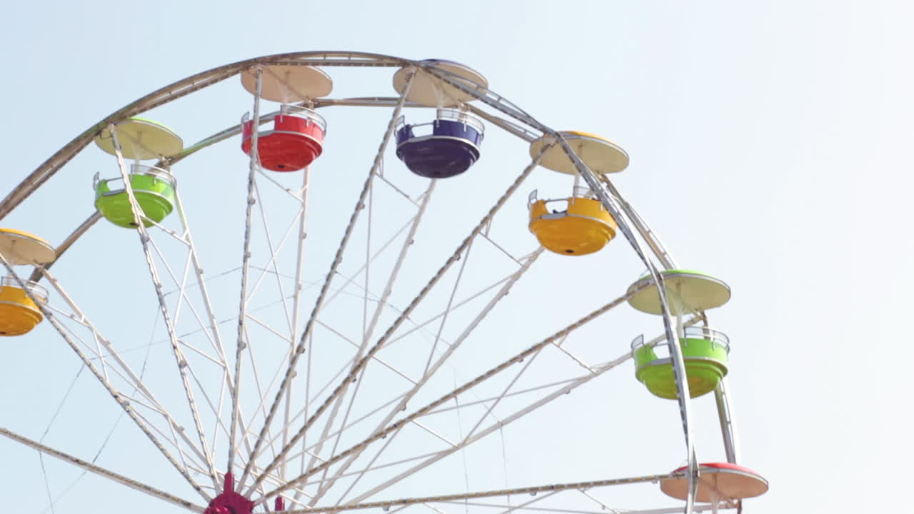 A Rainbow colored Ferris wheel spins around and around during a summertime music festival. The people are prepared to enjoy the ride in Chicago