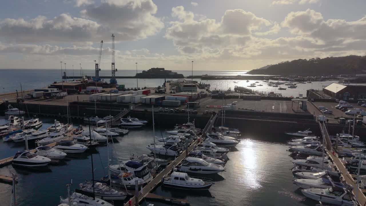 Volo radente al tramonto sopra la Marina e porto QEII 319 di St Peter Port, Guernsey, e North Beach, verso il Castello Cornet mentre il sole cala.