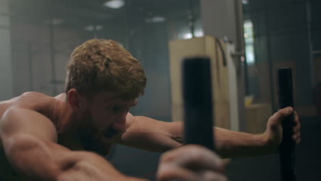 close-up: a tenacious purposeful male athlete pushes a heavy sled in the gym. exercise with a heavy weight for endurance. sports spirit of victory