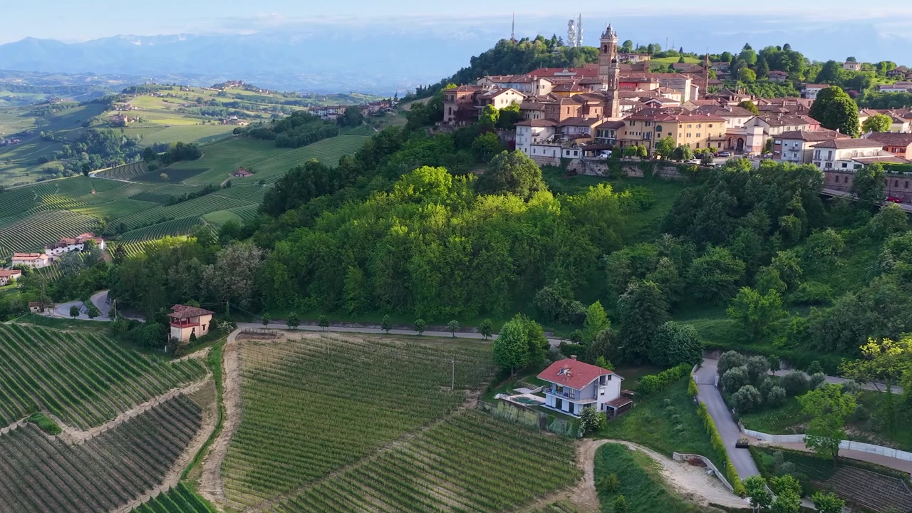 Ripresa aerea con drone dall'alto sorvola dolci colline vitate verso un borgo storico italiano.