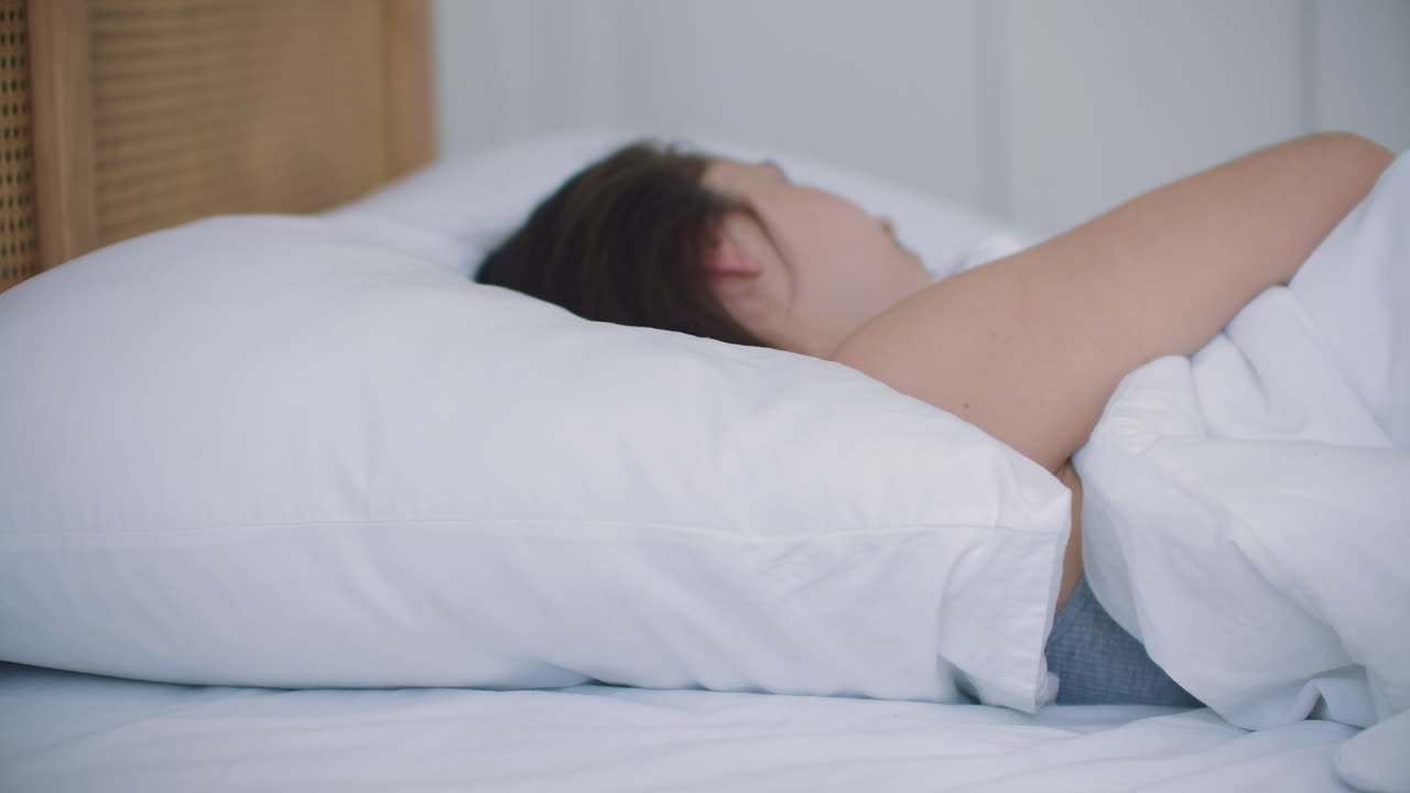 잠옷을 입은 매력적인 갈색 여성이 침대에 누워 잠을 못 자고 있습니다.