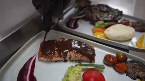 el chef vierte salsa barbacoa sobre salmón a la parrilla, comida en el restaurante, primer plano