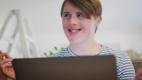 Young-Downs-Syndrome-Man-Sitting-On-Sofa-Watching-Laptop-At-Home-And-Dancing