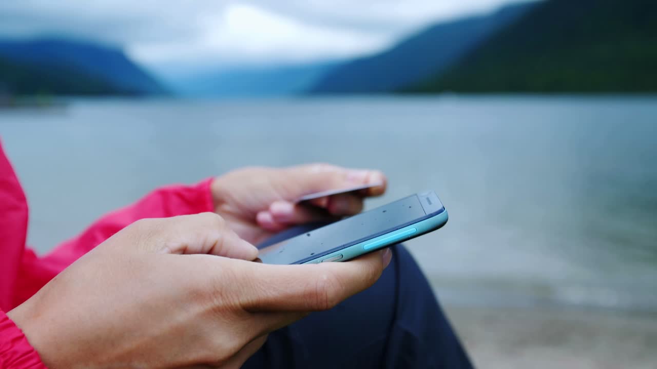 Person using smartphone and credit card by a lake