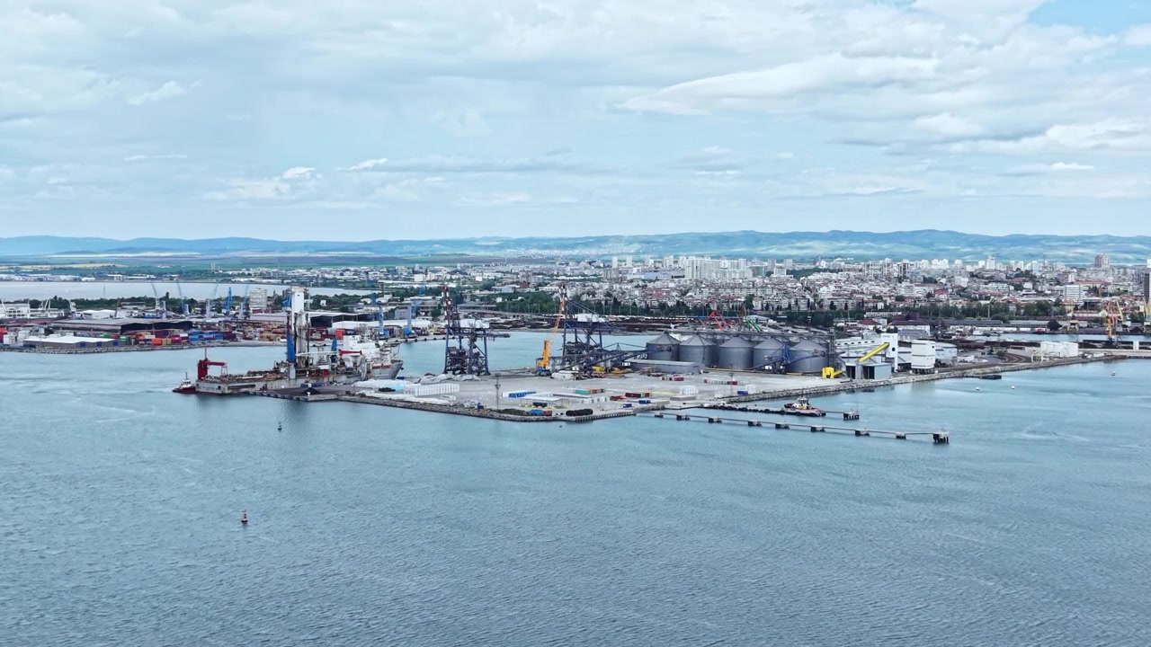 Öğleden sonra saatlerinde, bulutlu bir günde, su kenarındaki şehirde çeşitli gemiler, vinçler ve endüstriyel yapılarla dolu yoğun bir liman bölgesinin görünümü.