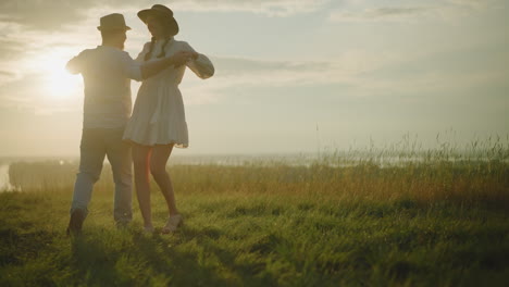 a romantic scene of two lovebirds dancing tenderly on a sunlit grassy hill, sharing a loving moment together. the man, dressed in a white shirt, hat, and jeans, holds his wife, who wears a white dress