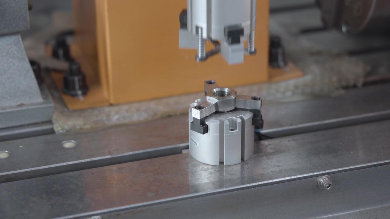 Metal clamping mechanism remains steady on steel worktable, with silver head and gray jaws centered low in view and gentle shifting that emphasizes worn rail texture, with industrial, machine