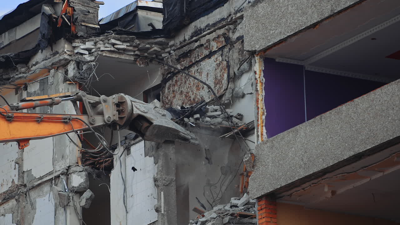 Demolition of the house previously destroyed by natural disaster. Special machinery breaks the parts of ruins. Dusty debris falling down the ground.