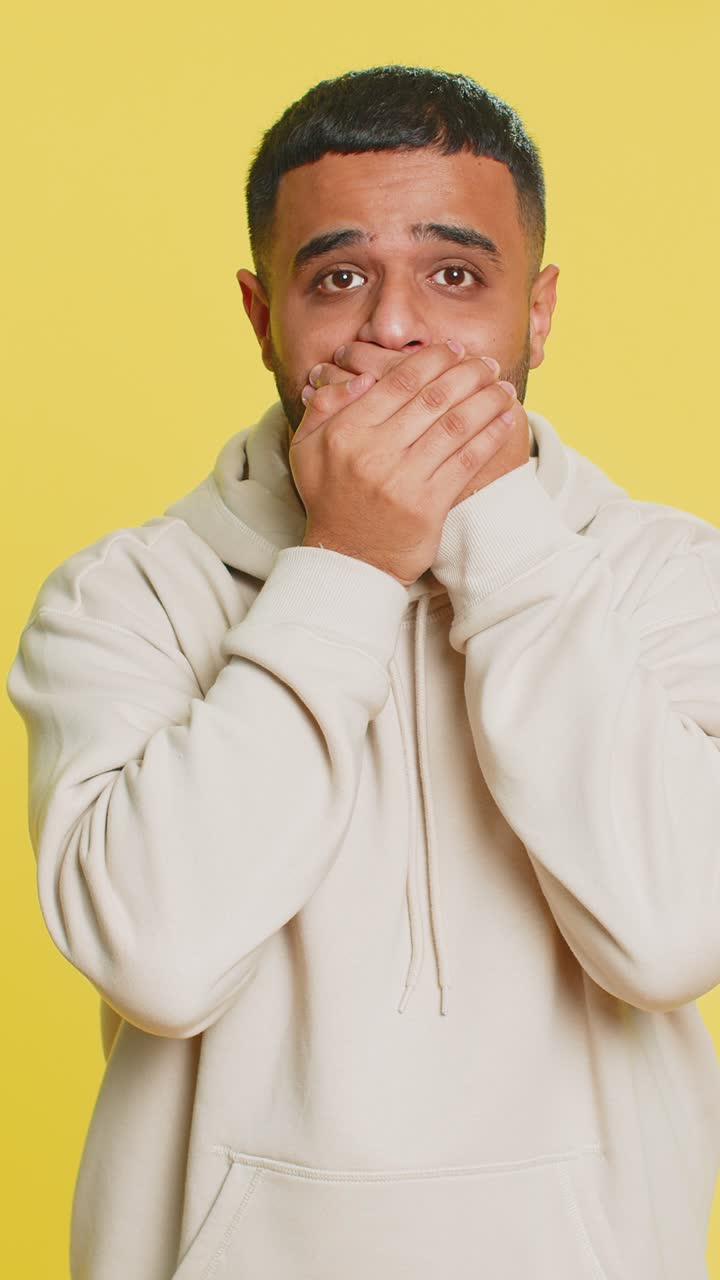 Frightened indian man closing mouth with hands refusing to tell terrible secret unbelievable truth