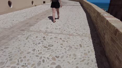 woman walking on a stone path in the village of grottammare in italy. ancient buildings and on the horizon the blue sky and the sea.