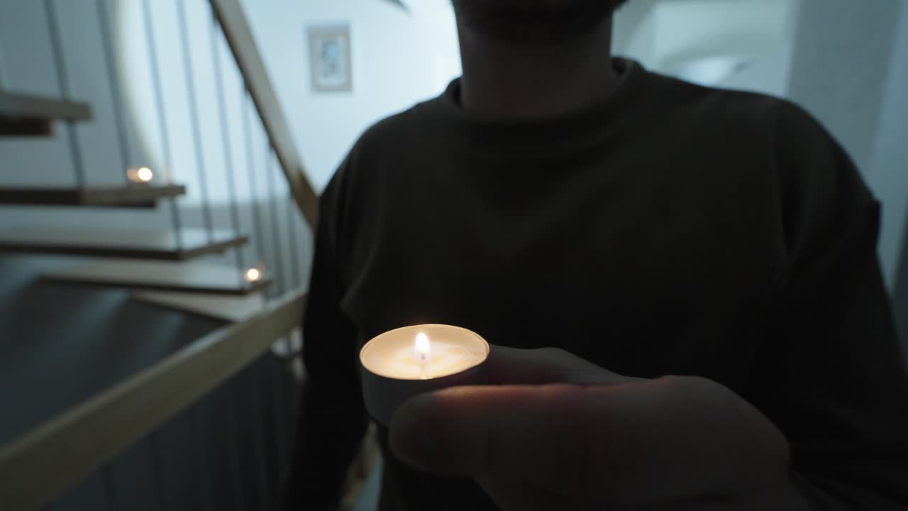 Hænder tænder et lille lys i et mørkt hjem under en blackout, hvilket skaber et varmt nødlys og en følelse af beredskab