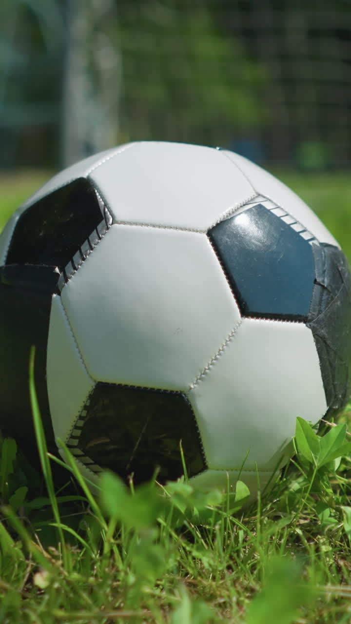 Close-up view of a soccer ball resting on a grassy field with a blur view of a little child running with a ball in his hand in the background