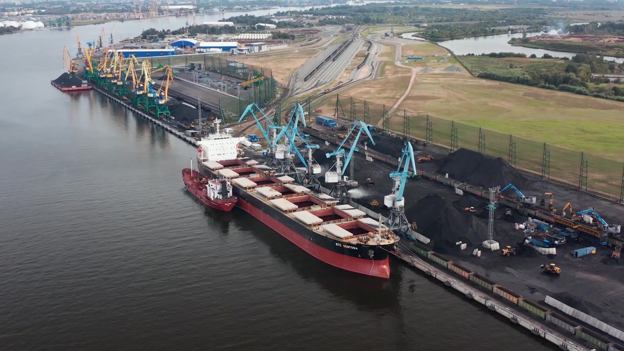 Aerial drone panorama view of coal transshipment to cargo ship. Loading with large cranes. Port district in the background. Rotating to left. 4k footage.