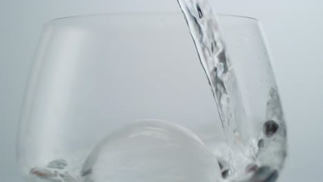 water pouring over round ice cube and berries in wine glass