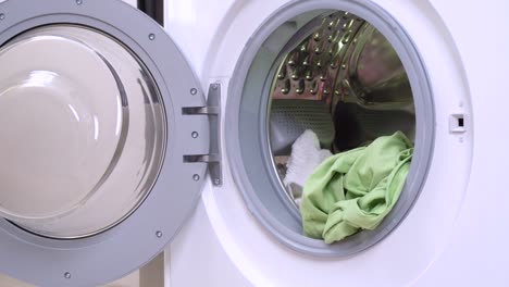 little black and tan dachshund wearing funny pink and white checkered housemaid costume and golden blond wig uploads laundries into opened washing machine drum. humor concept of pet housekeeping.