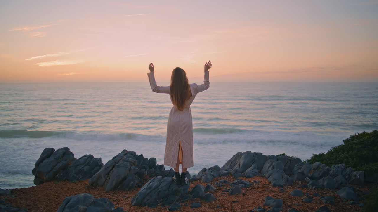 Serene girl enjoying sunset nature raising hands back view. Woman looking marine