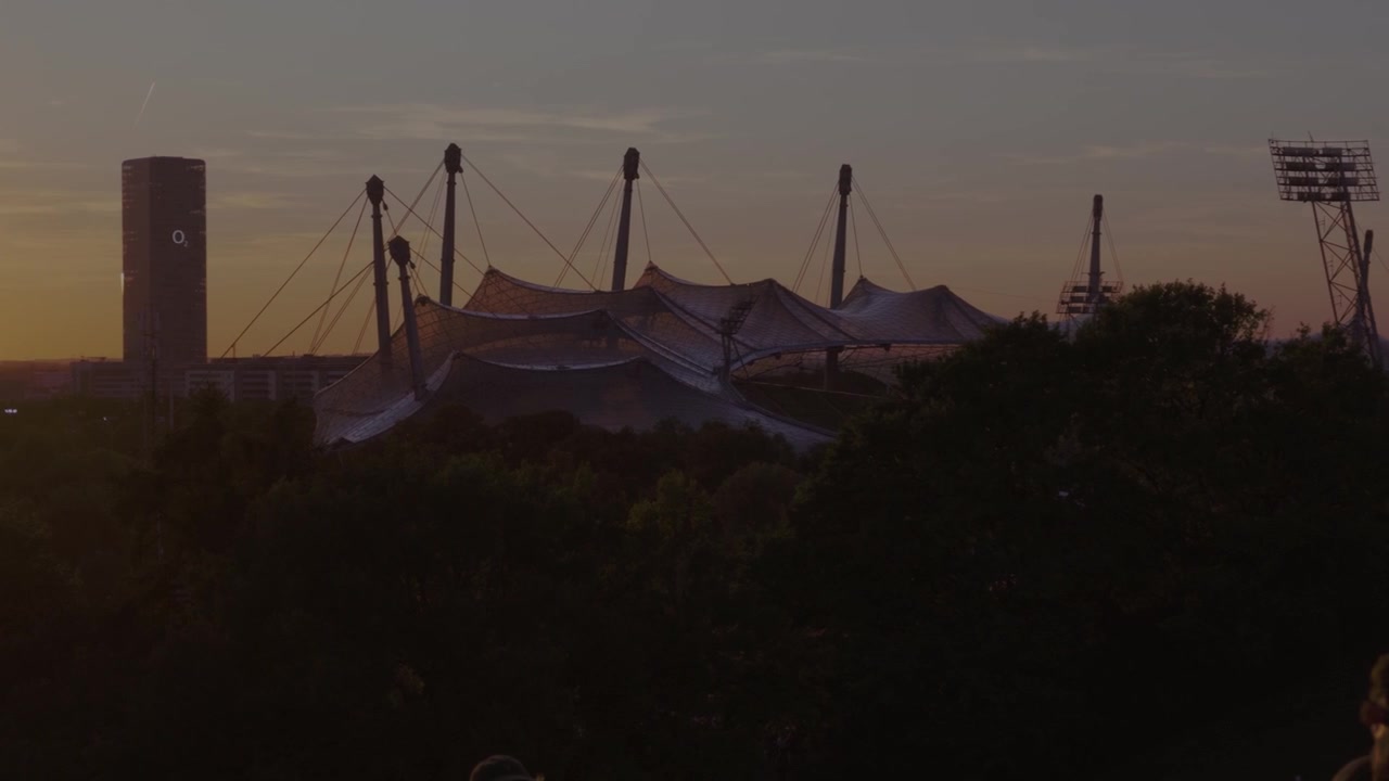 Silhouette of Olympic Stadium towers and ferris wheel against a darkening solar eclipse horizon in Munich