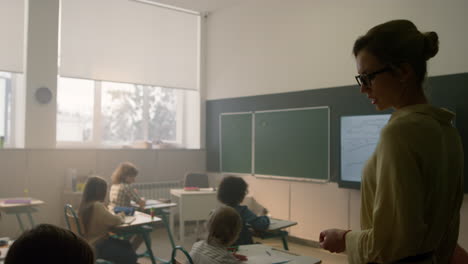 Teacher-talking-to-students-in-classroom.-Schoolchildren-studying-together