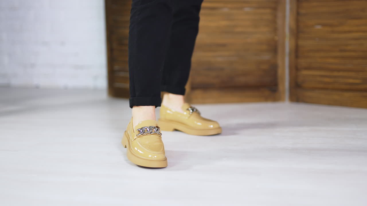 Beige comfortable shoes on a female model wearing black jeans. Demonstrating new loafers with silver chain decoration.