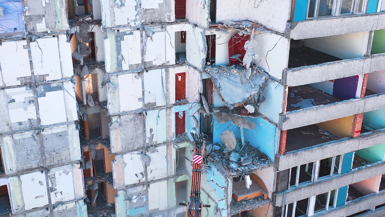 Demolishing machine breaks the walls and floors of the big ruined building. Aerial view of the deconstruction site.