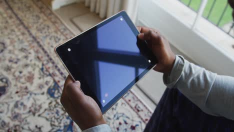 mid section of african american man holding a digital tablet with copy space at home