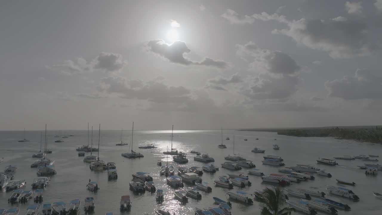 Drone view of moored boats in Bayahibe, Dominican Republic. Calm Caribbean waters and hazy sun create a peaceful tropical mood.