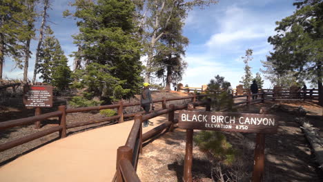 Black-Birch-Canyon-Viewpoint-Sign-in-Bryce-Canyon-National-Park,-Utah-USA-and-Woman-Walking-on-Path