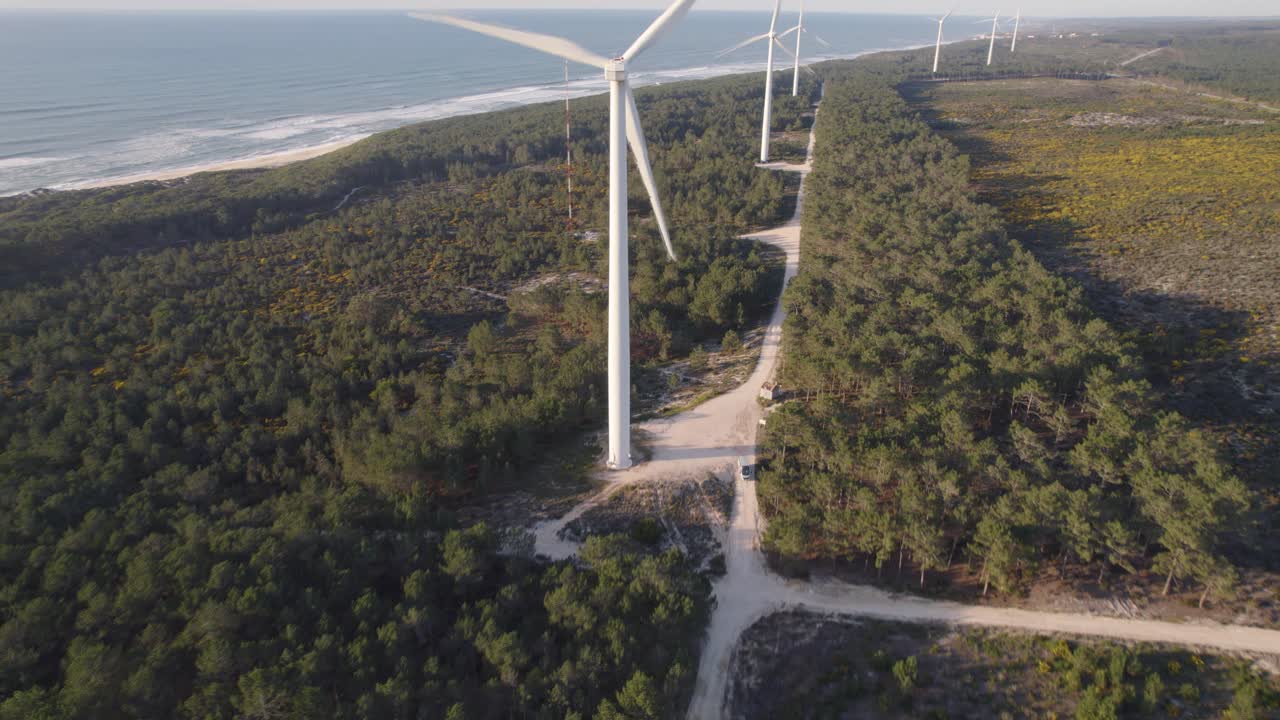 turbinas eólicas en el prado de nazare con olas aplastando la playa de arena en el fondo