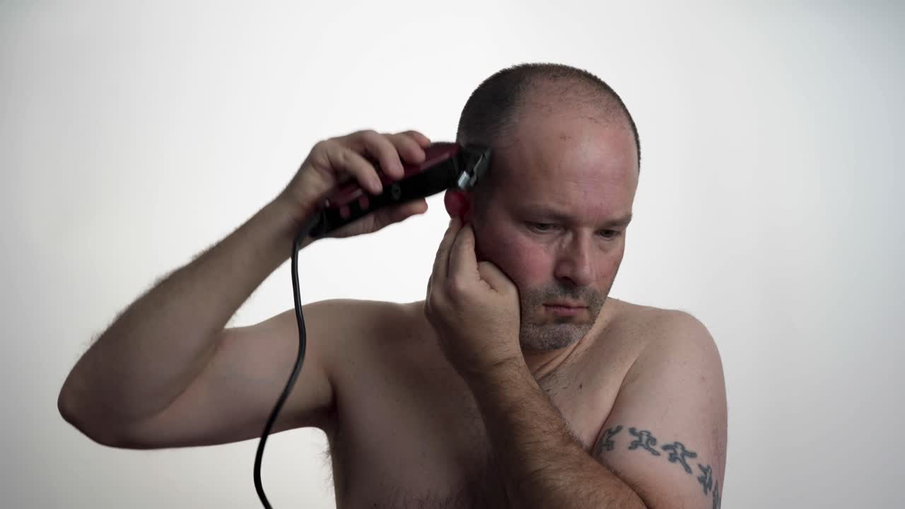 Man facing camera while he uses clippers to cut his own hair